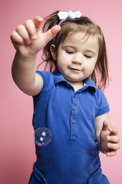Little girl smiling in studio playing with bubbles