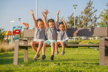 Hermanos amigos niños felices disfrutando y jugando levantando las manos combinados vestidos igual divertidos alegres sentados en una banca en parque infantil al aire libre