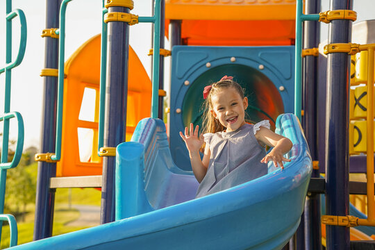 Ni&ntilde;a feliz jugando desliz&aacute;ndose en la resbaladilla en el parque al aire libre disfrutando de los juegos infantiles