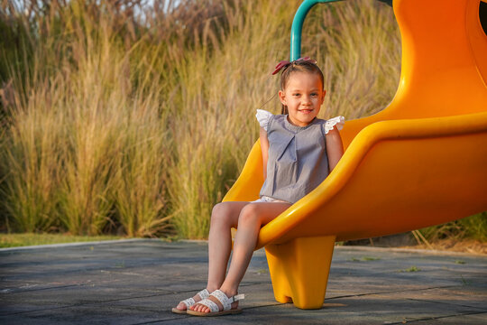 Ni&ntilde;a feliz jugando en parque contenta divertida disfrutando su infancia sentada en los juegos infantiles en una resbaladilla posando con una sonrisa