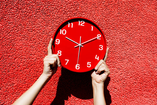 man holds a red clock against a red walk