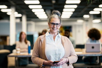 Smiling mature female manager browsing smartphone