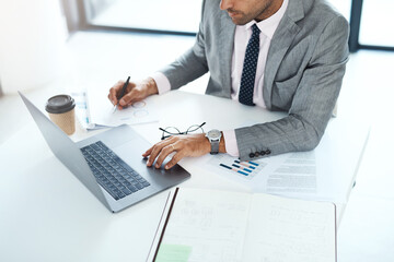 Working hard to earn harder. Cropped shot of a businessman working with paperwork and his laptop.