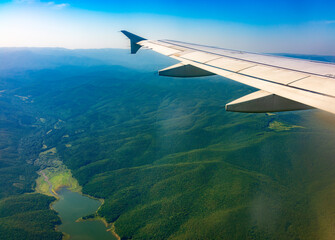 Obraz premium View of airplane wing, blue skies and green land during landing. Airplane window view.