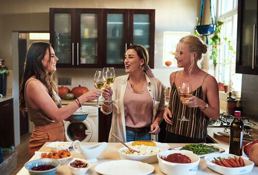 Heres to us girls. Cropped shot of a group of cheerful young friends having a celebratory toast with drinks while standing in the kitchen preparing food at home.