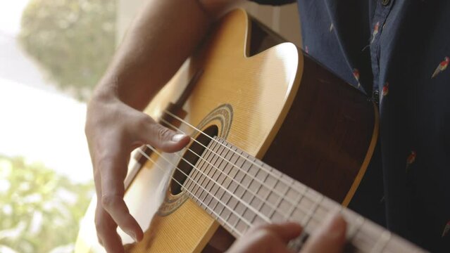 Close up slow motion shot of a person playing a guitar by fingerpicking.