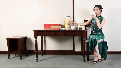 Beautiful young woman wearing modern Chinese style dress cheongsam fashion retro vintage table room drink tea