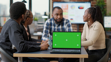 Team of african american people having laptop with green screen, working on financial strategy. Colleagues using chroma key template with isolated copy space and blank mockup background. Tripod shot.
