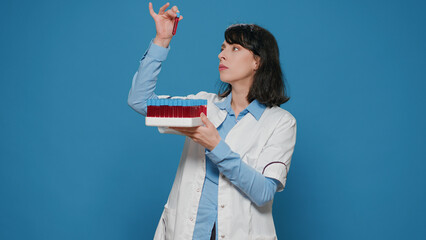 Female scientist analyzing test tubes on laboratory tray, looking at liquid substance in lab...