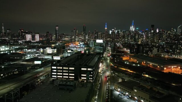 An aerial view high over Long Island City, New York at night. The drone camera dolly in and pan right slowly, taking in the east side of the beautiful NYC skyline.