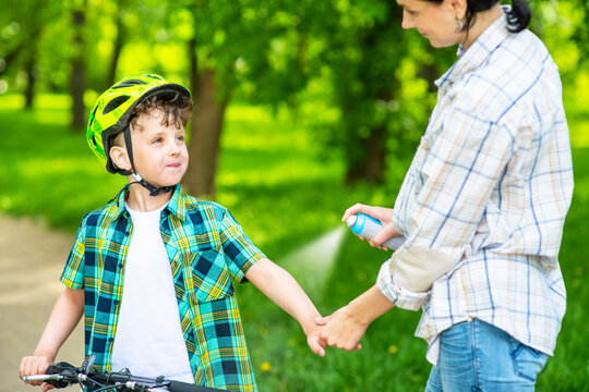Mom spraying repellent on the skin of a smiling and looking son to protect against mosquitoes while cycling in the park. Close-up image