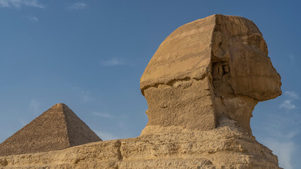 Sculpture of the Great Sphinx. Close-up. The head is visible in profile against the blue sky. The texture of sandstone.  The top of the pyramid is far away. Egypt. Giza