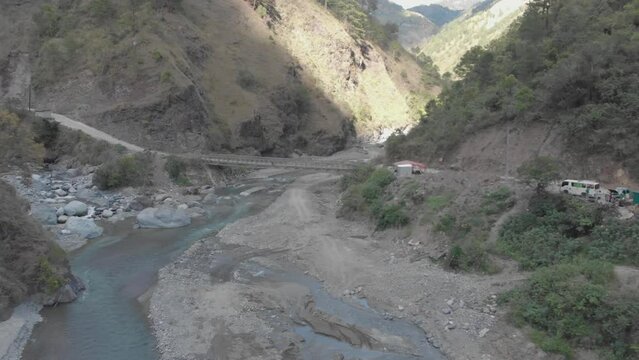 metallic bridge spanning over rocky river bed in mountainous valley surrounded by mountains trees bushes brush rocks dust in Kabayan Benguet Philippines high wide fast aerieal approach