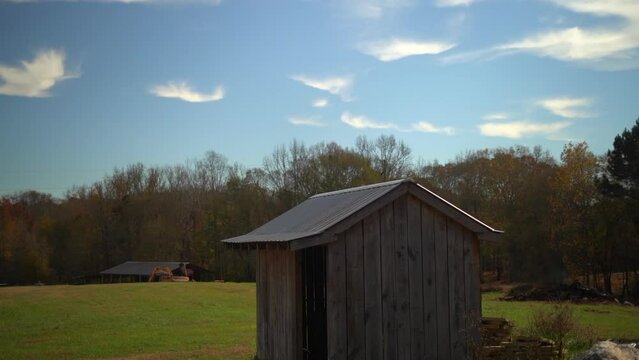 Majestic bluebird flies off of a mysterious wooden farming shed on a bright sunny afternoon - pan down and shot