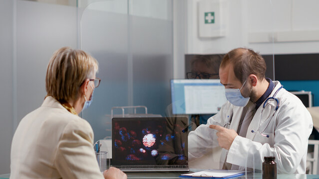 Health specialist showing virus illustration on laptop to old woman, explaining coronavirus danger and disease diagnosis. Retired patient and doctor with face mask at checkup visit. - Powered by Adobe