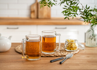 Two cups of tea with teapot and dry herbal flowers on a wooden countertop against the background of a white kitchen in the early morning. Healthy breakfast concept