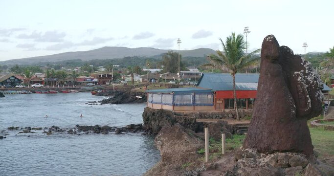 Sunset at Hanga Roa bay on Easter Island during magic hour as surfers and clouds pass by.