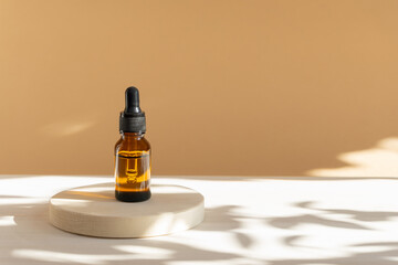 Unmarked amber glass bottle with dropper lid on beige background with floral shadow. Mock-up of facial serum in rays of sunlight. Close-up, copy space