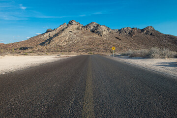 Fototapeta na wymiar Road and mountains in the Baja, near the sea of cortes in the state of Baja California Sur, in Mexico. horizontal landscape with blue sky in a hot summer afternoon travel and destination concepts.