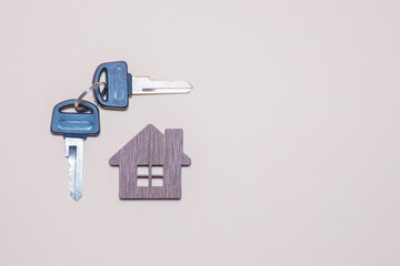 Door keys and wooden miniature of a residential building on grey or gray background: finding your own house, real estate agency and buying real estate