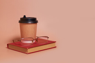A paper cup of coffee and glasses lie on a book on a colored background