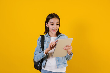 portrait of young hispanic child teen girl student with digital tablet on yellow background in...