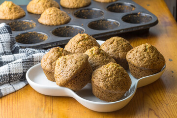 Freshly baked homemade muffins in white serving plate  and a baking tin on the table. Tasty sweet breakfast, homemade cakes.