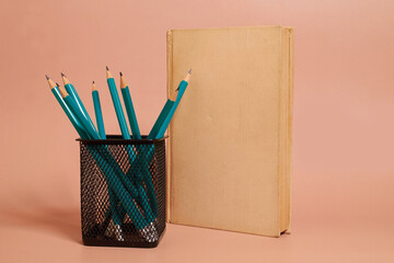 A glass with graphite pencils stands next to a book on a colored background