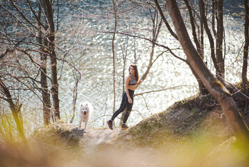 Woman in sport clothing exercising near lake with white dog