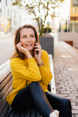 Happy elderly woman with beautiful face sitting on park bench takes phone call