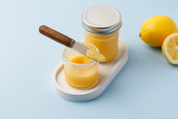 Jam with lemon in jar. Lemon curd with knife. Dessert with fresh lemon on tray. Blue background