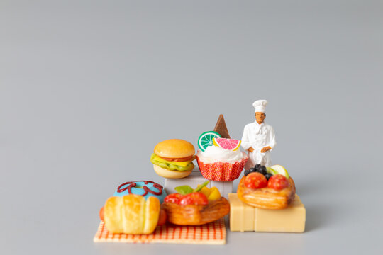 Miniature people , Baker standing with Sweet dessert on grey background