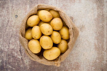 Sack of fresh raw potatoes on wooden background, top view.