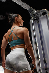 Muscular woman in gym showing back muscles. Strong fitness girl working out.