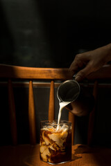 Ice coffee on a wooden table with cream being poured into it showing the texture and refreshing look of the drink