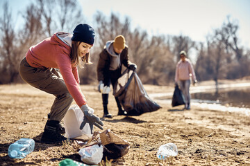 Young teenage girl with volunteers cleans trash on the beach.
