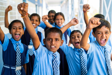 Group of cheerful students shouting by looking camera at school corridor - conept of innocence,...