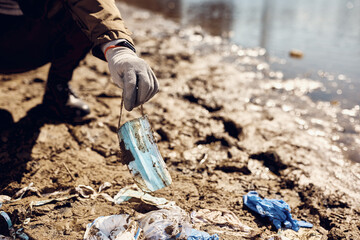 Close-up of man picking up dirty face mask while cleaning garbage on beach.