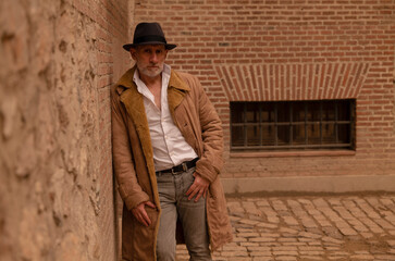 Portrait of adult man in hat and coat against brick wall on street. Madrid, Spain