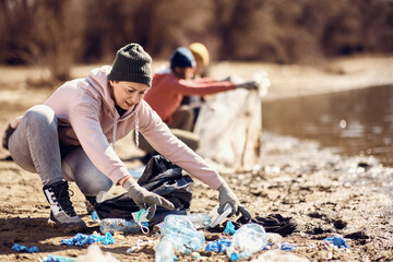 Female environmentalist picking up trash while cleaning lake shore with her friends.