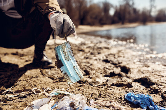 Close-up of man collecting used protective face masks while cleaning beach area.