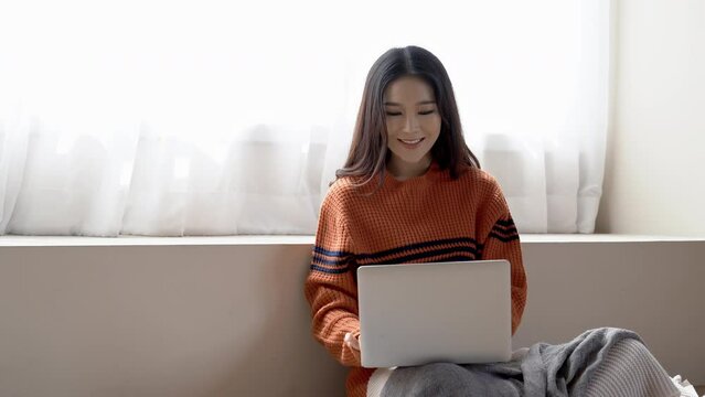 Portrait of happy freelancer Asian girl using laptop computer while sitting in cozy on floor at home in winter. Korean or Japanese Girl working from home, Cozy office workplace concept.