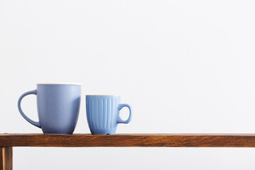 two blue cups on wooden shelf on white background