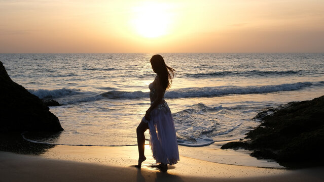 Woman looking at the sun at sunset on the beach stylized in belly dancer clothes. Woman dances to the sun wearing arabic dance costume. Fertility concept. Exotic beauty.