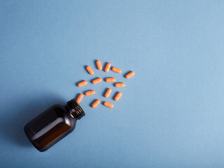 Pills spilling from a amber bottle, on blue paper background