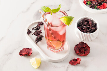hibiscus rose petal iced tea in a glass with pieces of ice and lime in a glass on a plaster tray and marble table. natural antibiotic and antiseptic.