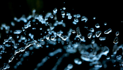 Drops of water splash blue water on a black background, concept of freshness drink, watering the rain source of pure water fountain copy space