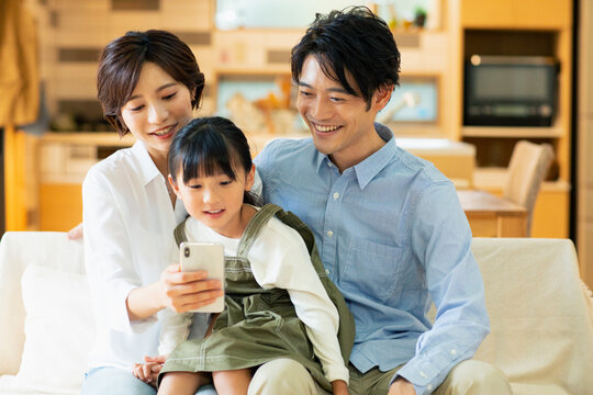 ソファーでスマートフォンを見ながらくつろぐ家族