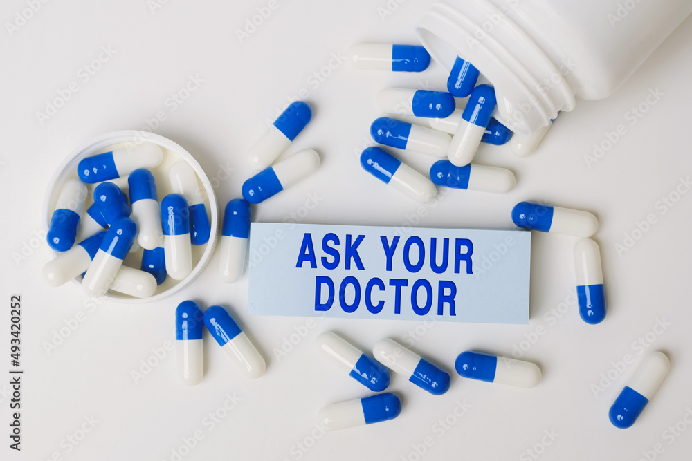 Wall mural ASK YOUR DOCTOR, inscription on paper note near blue-white pills spilling out of pill bottle. Medical concept