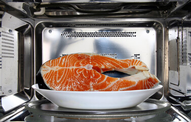 Raw fish in plate defrosting using microwave oven in close up